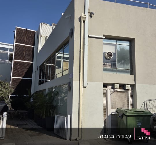 בניין עם חלונות גדולים ופח אשפה ירוק בחזית
